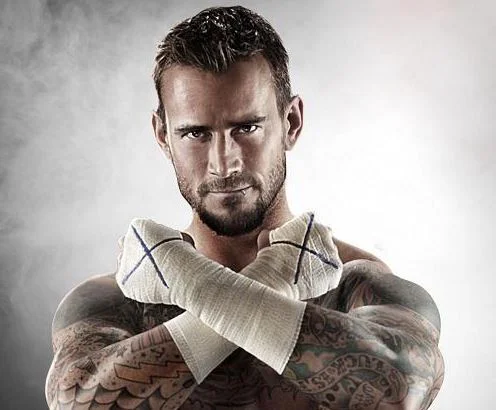 CM Punk shirtless with taped hands crossed in front of his chest, showing sleeve tattoos