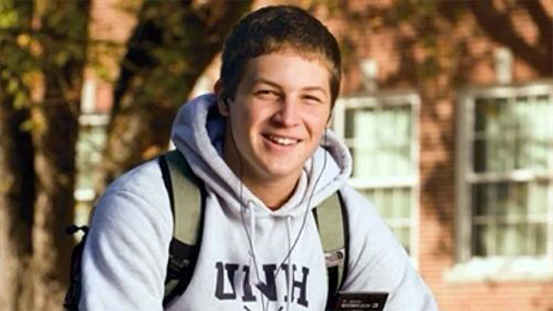 College Freshman — Smiling young man in white UNH hoodie with earbuds and backpack on a college campus
