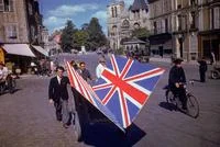 Colorized History — Colorized men carrying vivid Union Jack flag through European town square during WWII.