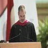 Commencement Speeches — Speaker in black graduation robes at podium during outdoor ceremony with tent.