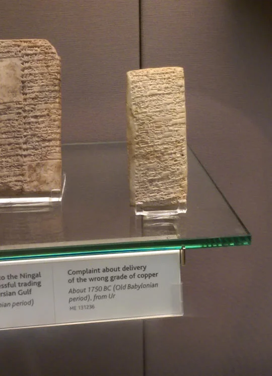 Complaint Tablet to Ea-nasir — Close-up of the Babylonian cuneiform complaint tablet in a museum display case with explanatory placard.
