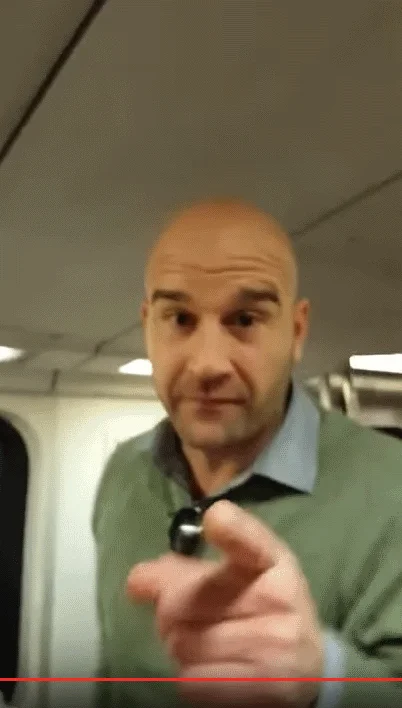 Conductor We Have A Problem! — Bald man in a green sweater pointing at the camera inside a subway train car.