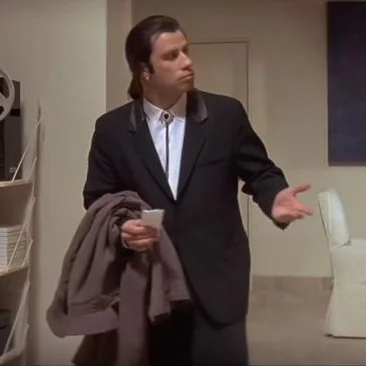 Confused Travolta — John Travolta in a black suit from Pulp Fiction, holding a jacket over one arm while gesturing outward in a bewildered shrug with apartment