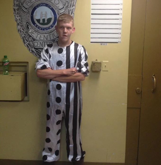 Creepy Clown Sightings — Young man in clown costume standing for mugshot at detention center