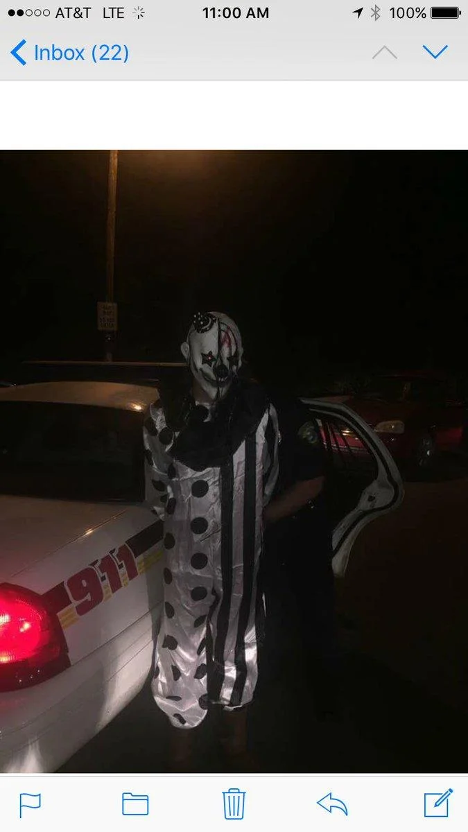 Creepy Clown Sightings — iPhone screenshot showing photo of clown next to 911 police car at night