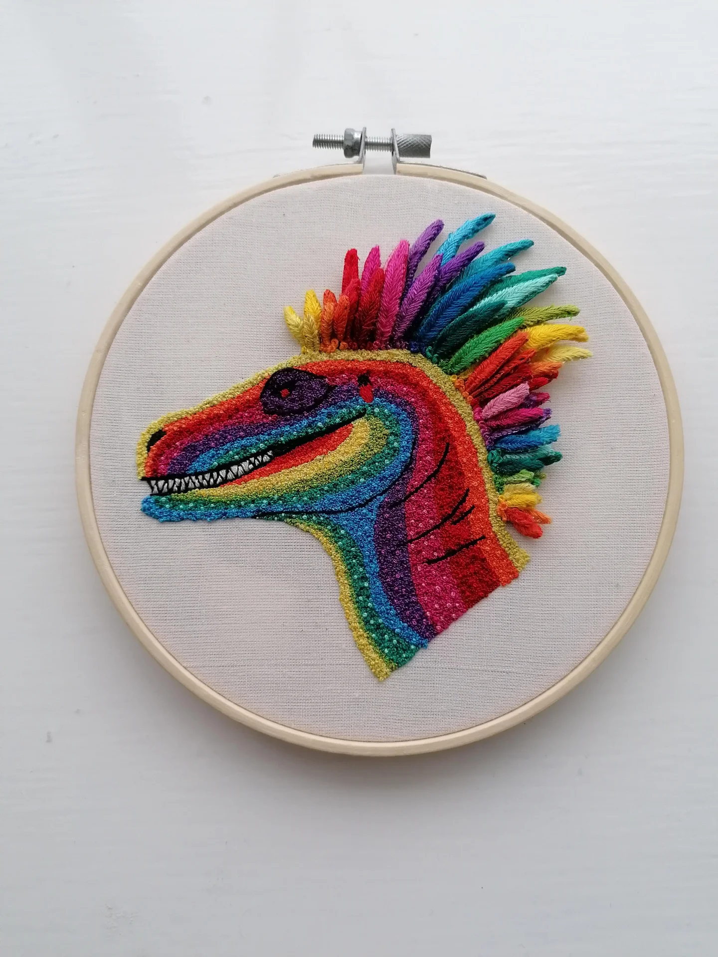 Cross-Stitch Art — Embroidery hoop art of a rainbow-colored dinosaur with a vibrant 3D mane