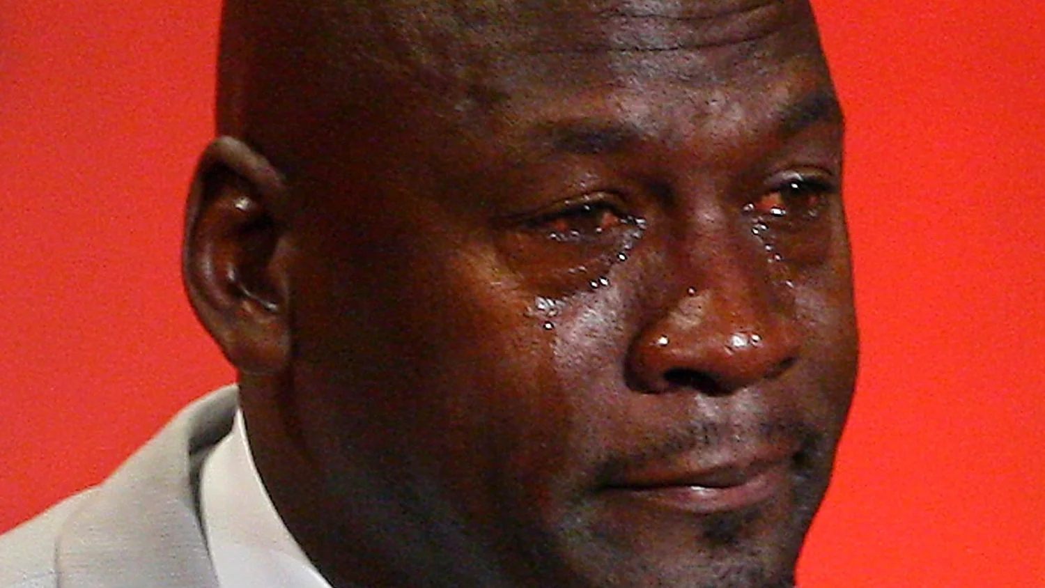 Crying Jordan — Close-up of Michael Jordan's emotional face with visible tears against bright red background.