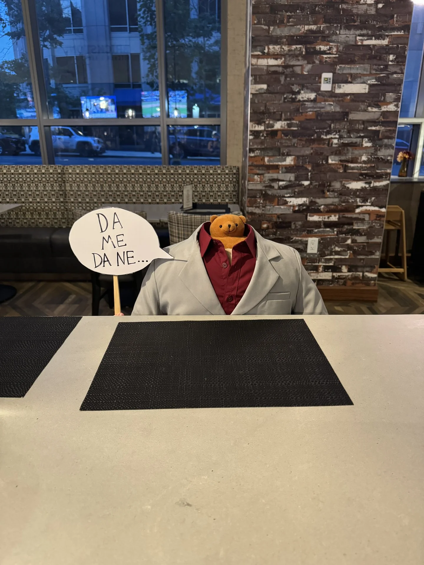 Teddy bear headed cosplay in Kiryu's white suit holding a 'Dame Da Ne' speech bubble sign
