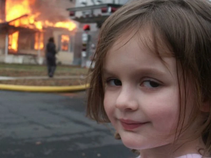 Disaster Girl — Original 2005 photograph with young girl's characteristic mischievous smirk facing camera with burning house background.