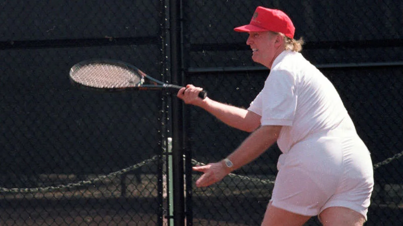 Donald Trumps Tennis Photo — Donald Trump in red cap and white tennis outfit swinging a racket on a court
