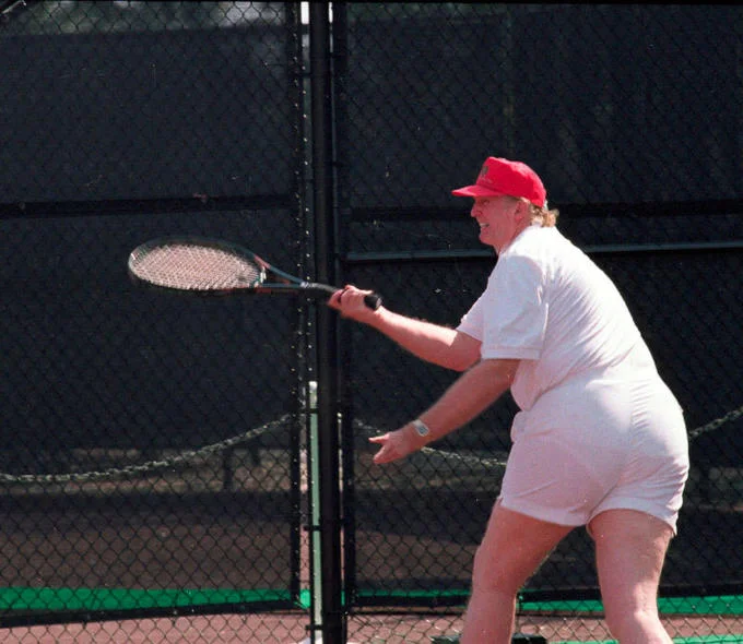 Donald Trumps Tennis Photo — Donald Trump playing tennis in white outfit and red cap, mid-swing