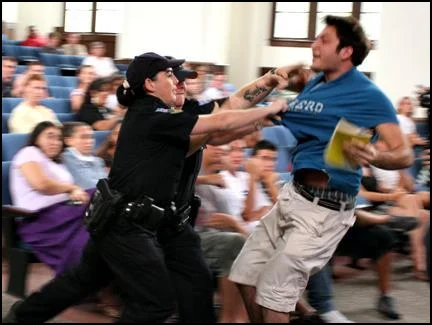 Dont Tase Me Bro — Photograph of Andrew Meyer in blue shirt being forcibly held by uniformed security with audience visible in background.