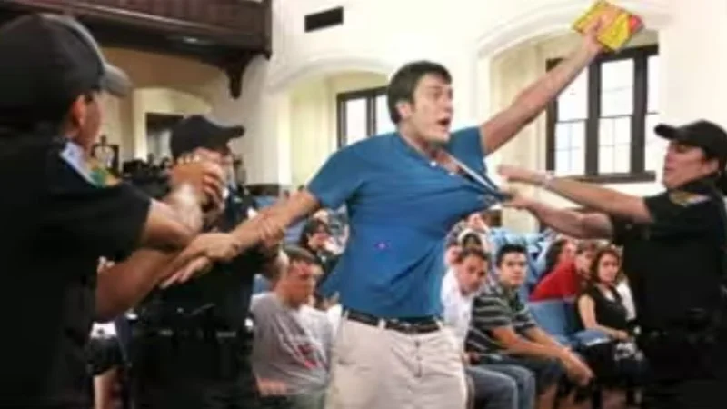 Dont Tase Me Bro — High-resolution photograph of Andrew Meyer with raised fist confronted by multiple uniformed security personnel.