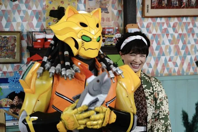 Eat Salmon On Christmas — Yellow-orange robotic monster character posing with laughing woman in Japanese clothing.