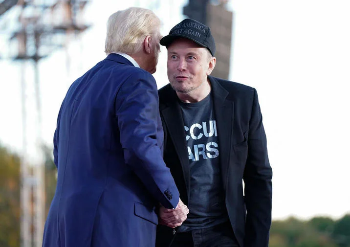 Elon Musk Kubrick Stare — Elon Musk in black MAGA hat shaking hands with Donald Trump at outdoor rally.