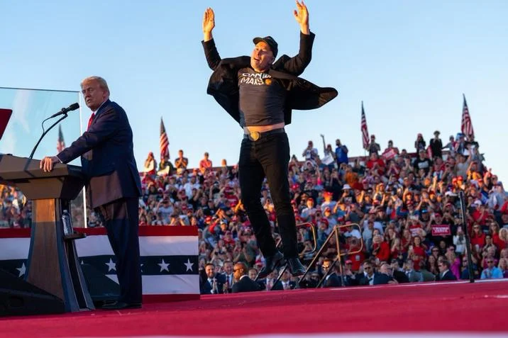 Elon Musk Memes — Elon Musk jumping with arms raised at Trump rally in daylight.