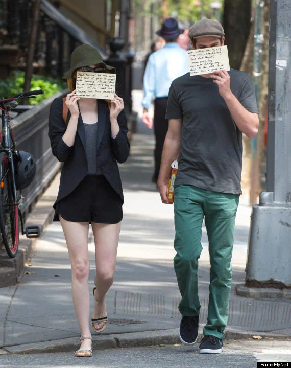 Emma Stone and Andrew Garfield holding cardboard signs promoting charities