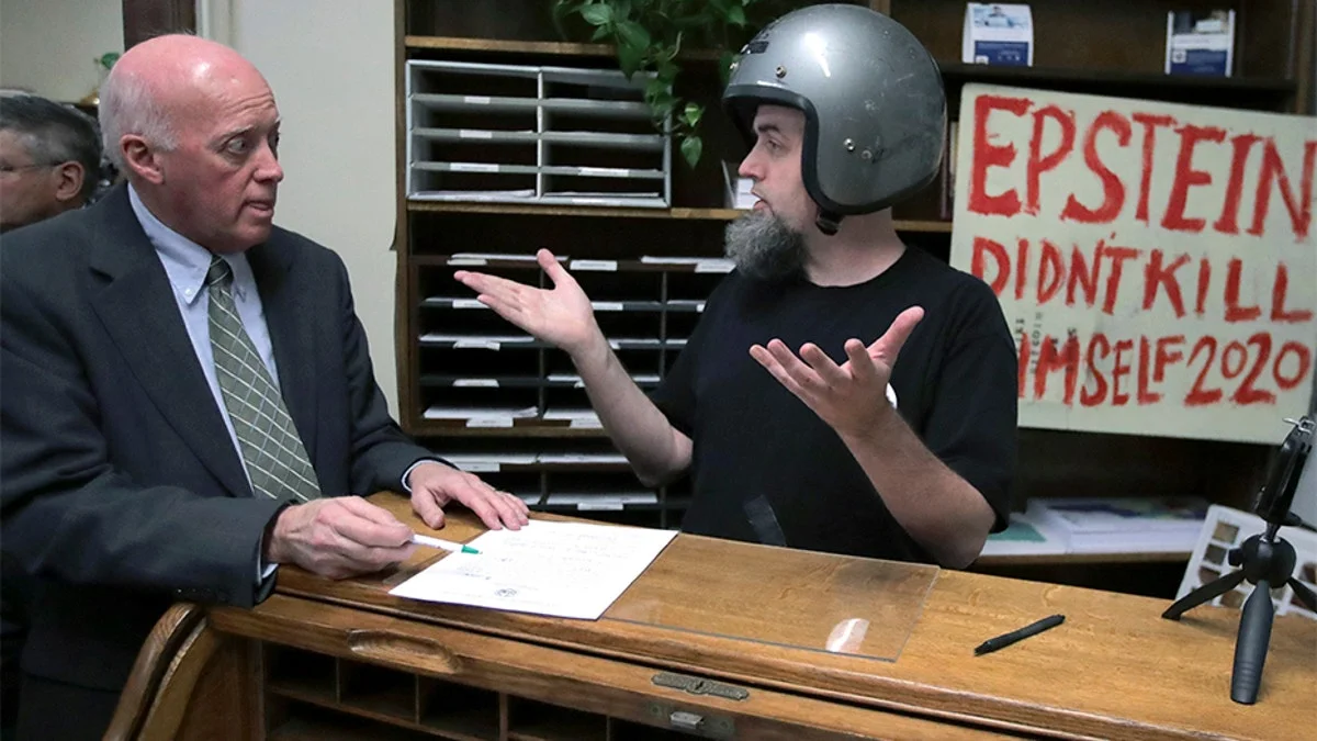 Interview scene with handmade sign reading 'EPSTEIN DIDNT KILL HIMSELF 2020' visible.