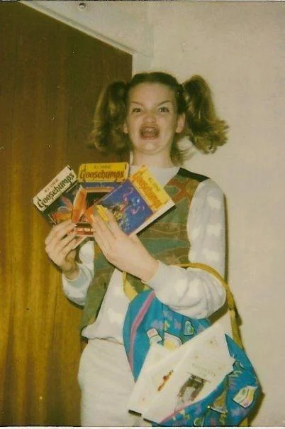 Ermahgerd — Girl with pigtails holding colorful snack packages with excited open-mouth expression.