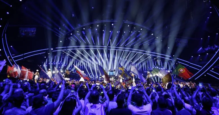 Eurovision Song Contest stage with blue lighting and audience waving national flags