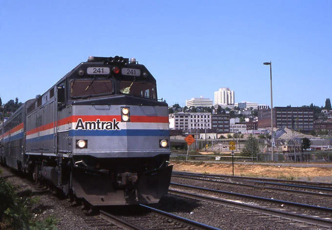 Amtrak F40PH locomotive 241 pulling a passenger train through a city rail yard