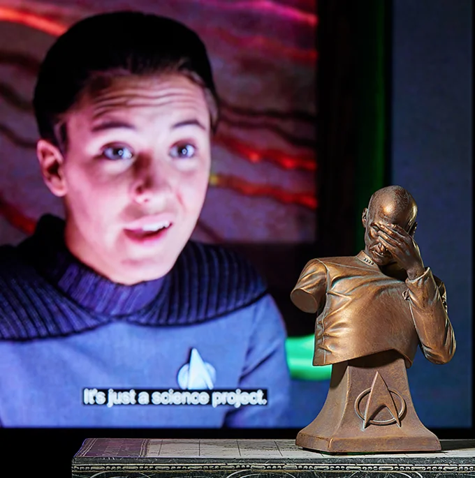 Facepalm bust displayed in front of TV screen playing Star Trek scene.