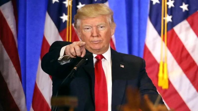 Fake News 3 — Trump pointing emphatically at lectern with American flags during press conference.