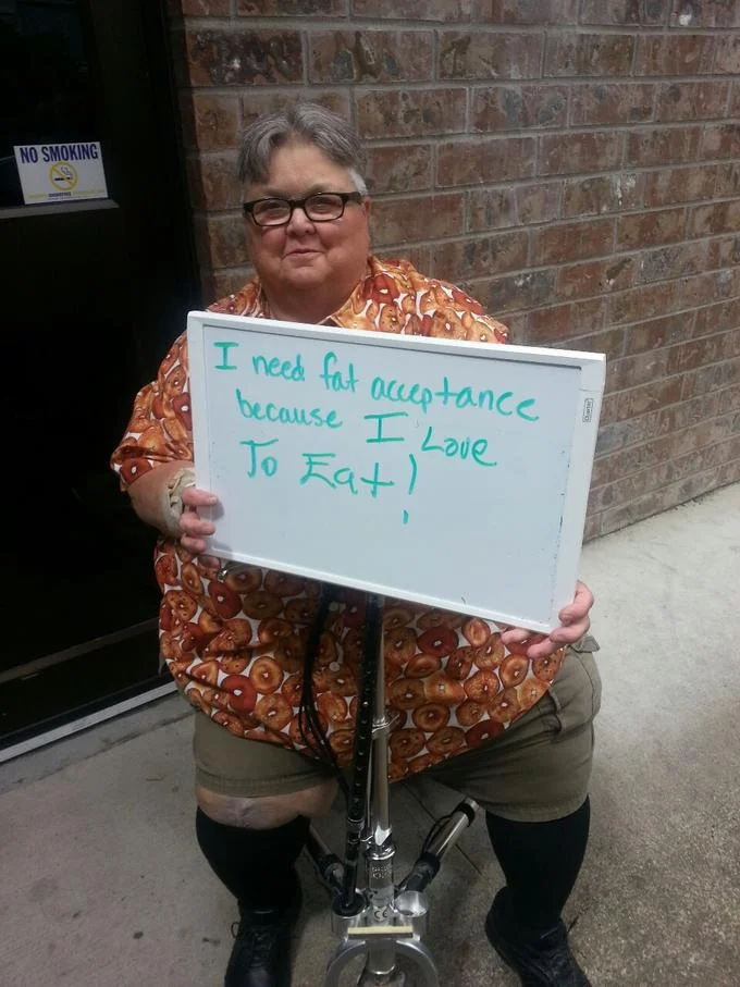 Fat Acceptance Movement — Older woman on knee scooter holding fat acceptance sign about loving to eat