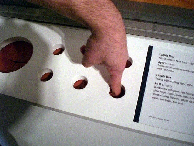 Finger Boxes — Museum display of AY-O Finger Box with a hand inserted into one of several circular openings.