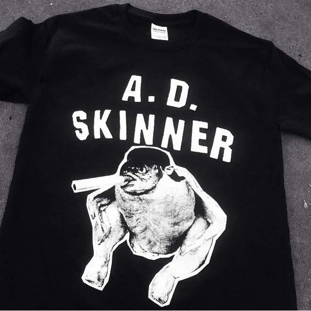 Fish Chicken Smoking A Cigarette — Black T-shirt with 'A.D. Skinner' text above a black-and-white drawing of a fish-headed chicken smoking a cigarette.