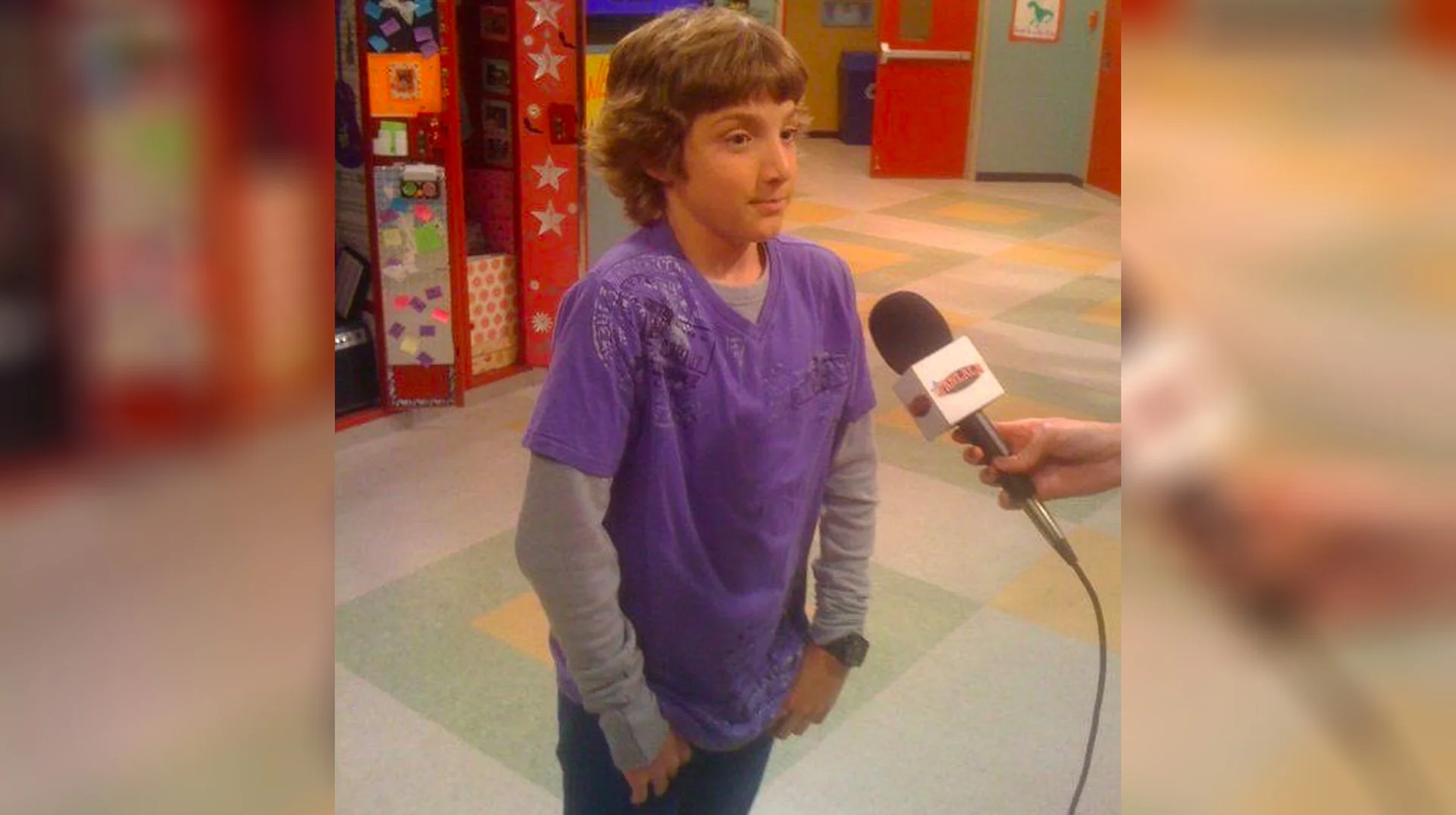 Fletcher Quimby Getting Interviewed — Boy in purple shirt being interviewed with a microphone in a school hallway