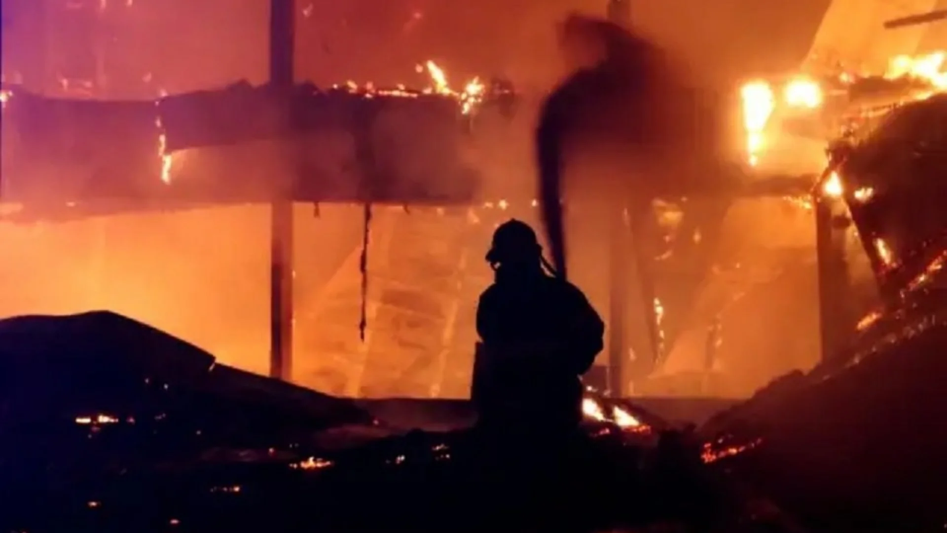 Food Processing Plants Fires Conspiracy Theory — Firefighter silhouetted against a large industrial fire at night
