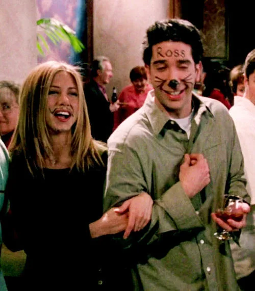 Friends — Rachel laughing with Ross whose face is drawn on with cat whiskers and 'ROSS' on his forehead