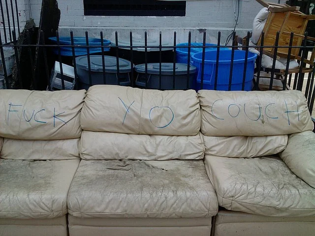 Fuck Yo Couch — Discarded brown patterned couch in an alley tagged with 'Fuck Your Couch'