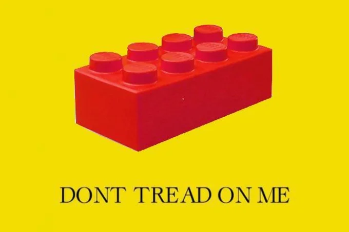 Gadsden Flag Dont Tread On Me — A bright red LEGO brick centered on yellow background with 'DONT TREAD ON ME' text below, substituting the snake with a toy