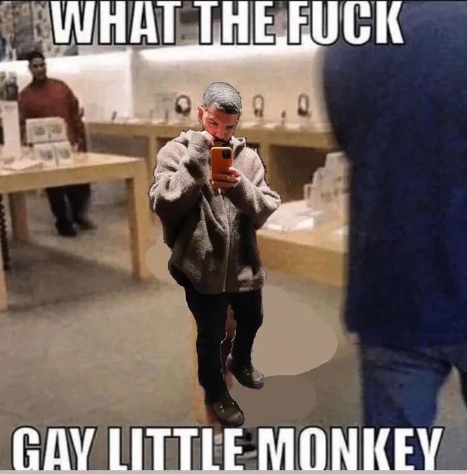 Gay Little Monkey Boy At Apple Store — Elderly character in beige coat standing in Apple Store with signature captions 'WHAT THE FUCK' and 'GAY LITTLE MONKEY.'
