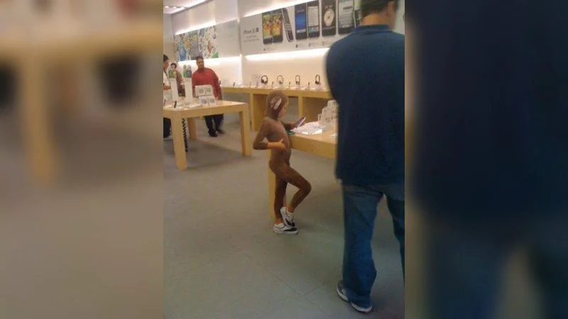 Gay Little Monkey Boy At Apple Store — Original source image showing a person in brown outfit standing in an Apple Store with white Apple product display