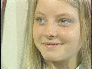 A blonde woman displaying a serene, subtle smile and composed demeanor, the iconic Gay Silence meme expression.