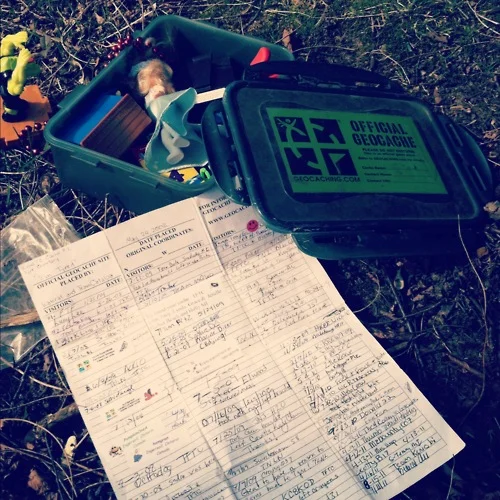 Geocaching — Opened geocache container with trinkets and a signed logbook
