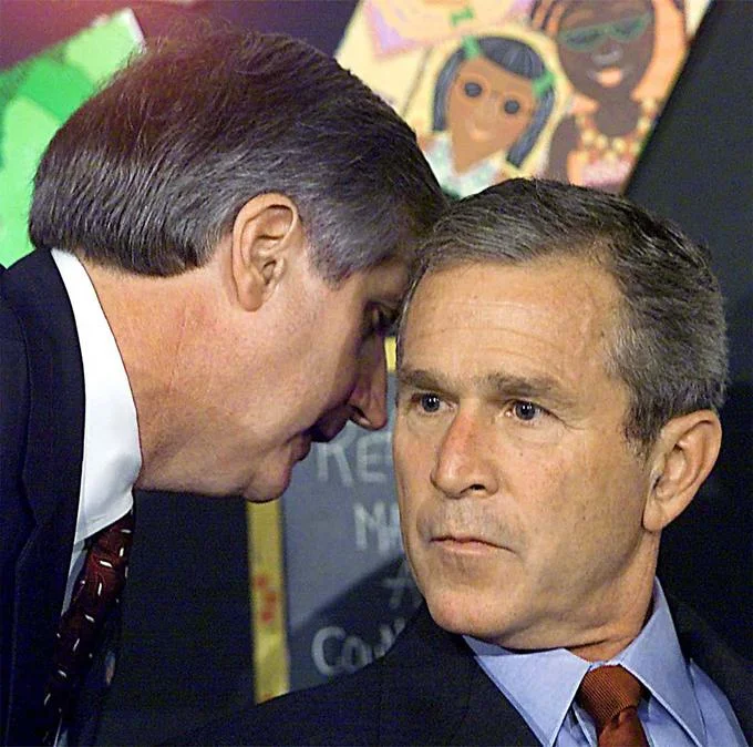 George Bush Learning About 911 — Andrew Card leans in to whisper into George W. Bush's ear inside an elementary school classroom.