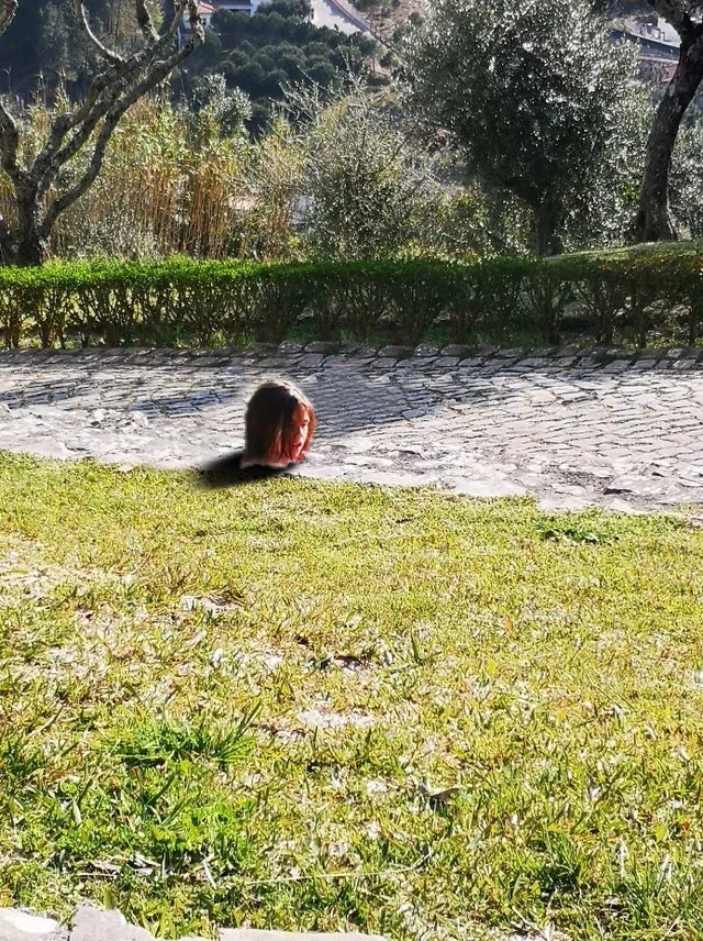 Girl Stuck In Concrete Illusion — Same outdoor location with only dark-haired head visible above grass line, exaggerating the submersion illusion.