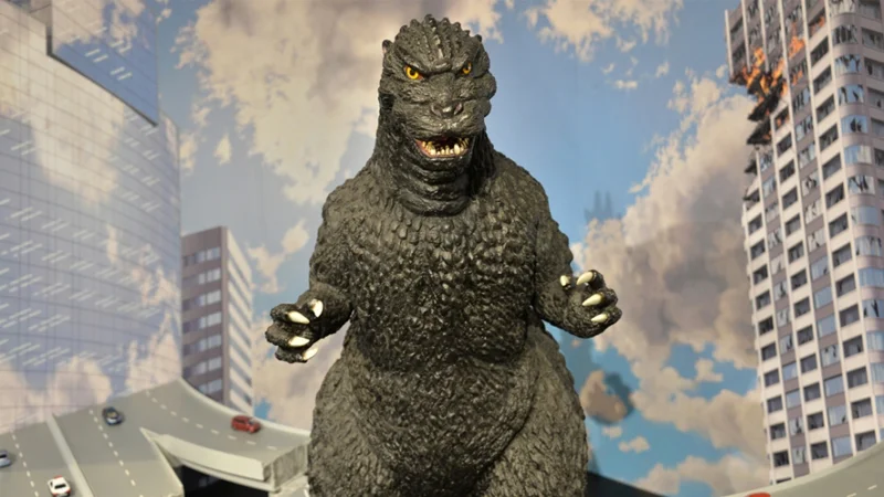 Godzilla figure standing in front of a cityscape diorama with a burning building