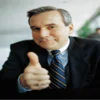 Quintessential Good Guy Boss image of businessman in dark suit and striped tie giving confident thumbs-up.