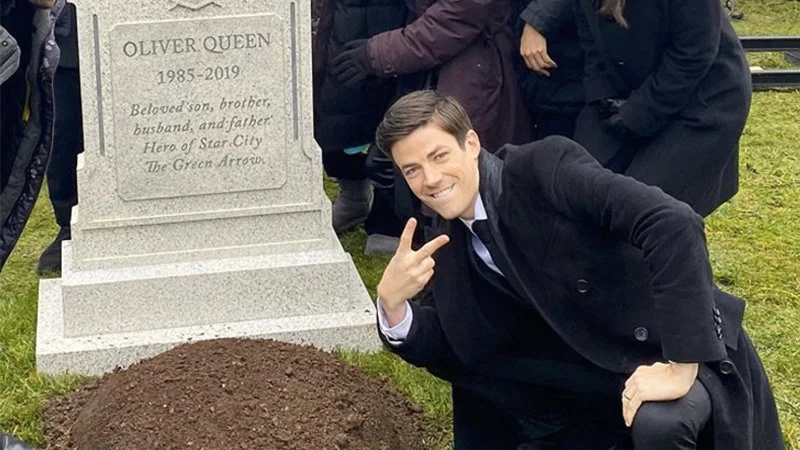 Grant Gustin Next To Oliver Queens Grave — Grant Gustin kneeling beside Oliver Queen's gravestone displaying peace sign.