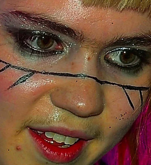 Close-up of Grimes wearing glittery eye makeup and painted face lines