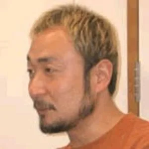 Guiles Theme Goes With Everything — Close-up profile photograph of Asian man with blonde-dyed hair wearing rust-colored shirt against beige wall.