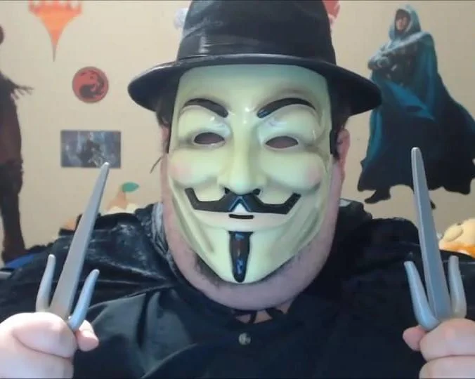 Person in Guy Fawkes mask and fedora holding Wolverine claws