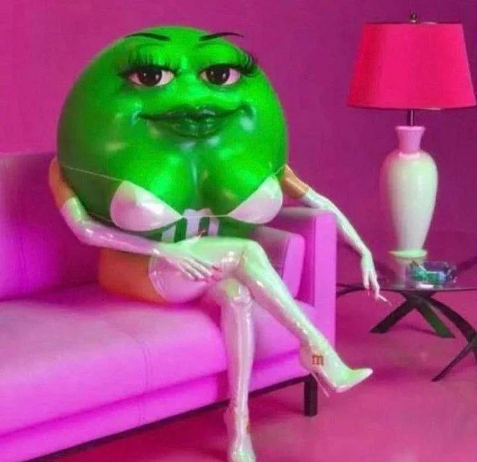 Haci Como Escuchaste — Original image of the green female M&M character sitting cross-legged on a pink couch