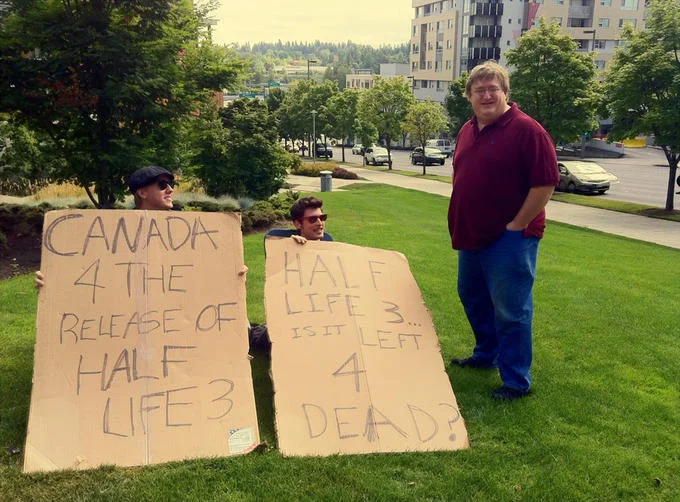 Fans holding Half-Life 3 protest signs next to Gabe Newell on a lawn