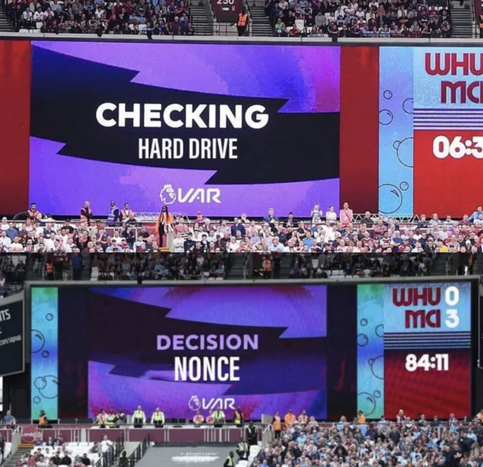 Hard Drive Check — Edited VAR big-screen graphic reading 'CHECKING HARD DRIVE' and 'DECISION: NONCE' at a football stadium